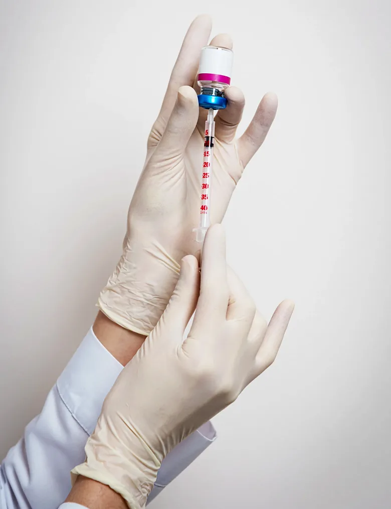 Imagem ilustrativa: mãos com luvas preparam uma seringa a partir de um frasco de medicamento
